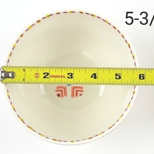 May include: A white ceramic bowl with a red and yellow patterned rim. The bowl measures 5-3/4 inches in diameter.