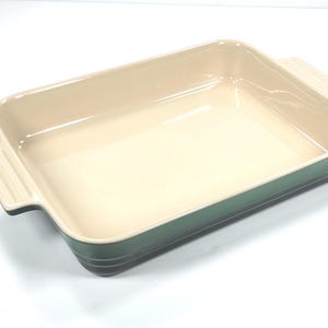 Könnte beinhalten: Rechteckige Backform aus Keramik mit cremefarbenem Innenraum und grünem Äußeren. Die Form hat zwei Griffe. Geeignet zum Backen von Aufläufen, Desserts und anderen Gerichten. Maße in Zentimetern.