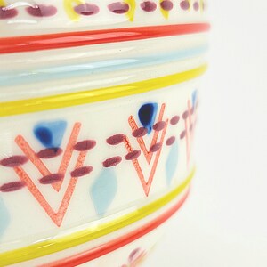 May include: A white ceramic bowl with a colourful geometric pattern. The pattern includes red, yellow, blue and pink stripes and triangles.