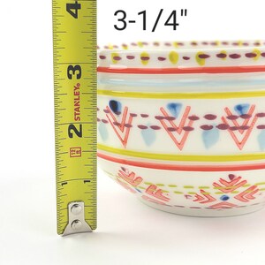 May include: A white ceramic bowl with a colourful geometric pattern. The bowl measures 3-1/4 inches in diameter.