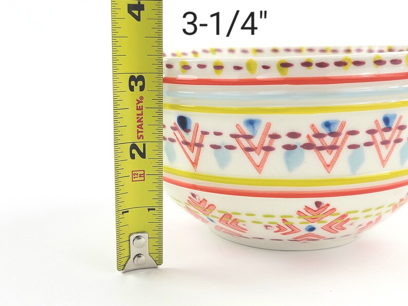 May include: A white ceramic bowl with a colourful geometric pattern. The bowl measures 3-1/4 inches in diameter.