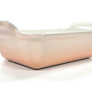 May include: A rectangular baking dish with a gradient color scheme, transitioning from a light peach at the base to white at the rim. The dish has two handles and is made of ceramic.