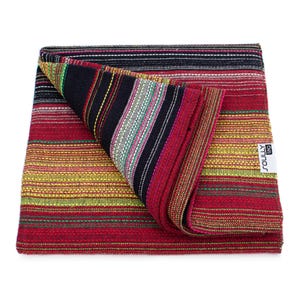 May include: A folded woven textile featuring a vibrant striped pattern in shades of red, yellow, black, and green. The fabric has a textured appearance with horizontal lines and a white rectangular tag with the text SOULLY tag attached to the side.