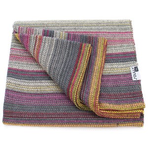May include: A folded woven blanket featuring a multi-colored striped pattern in shades of gray, magenta, yellow, and white. The fabric has a textured, interlaced weave throughout. A white rectangular tag with the black text SOULLY tag is attached.
