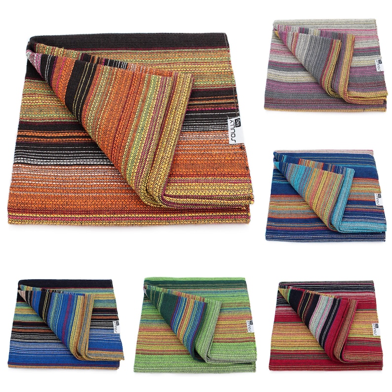 May include: A collection of six folded woven blankets featuring horizontal stripes in various color palettes including orange, black, blue, green, and red. Each blanket has a white rectangular tag with the text SOULLY printed in black.