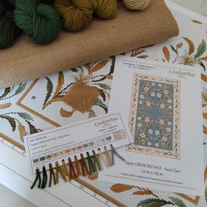 May include: A close-up of a cross-stitch kit with a colour chart and yarn samples. The kit is for a tapestry called "LIRIOS DO VALE - Azul Claro" and measures 1.10 metres by 1.85 metres. The kit includes a variety of colours, including green, brown, and white.