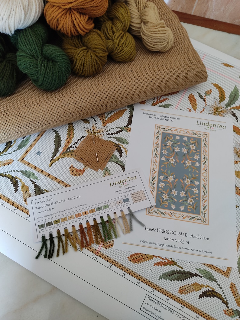May include: A close-up of a cross-stitch kit with a colour chart and yarn samples. The kit is for a tapestry called "LIRIOS DO VALE - Azul Claro" and measures 1.10 metres by 1.85 metres. The kit includes a variety of colours, including green, brown, and white.