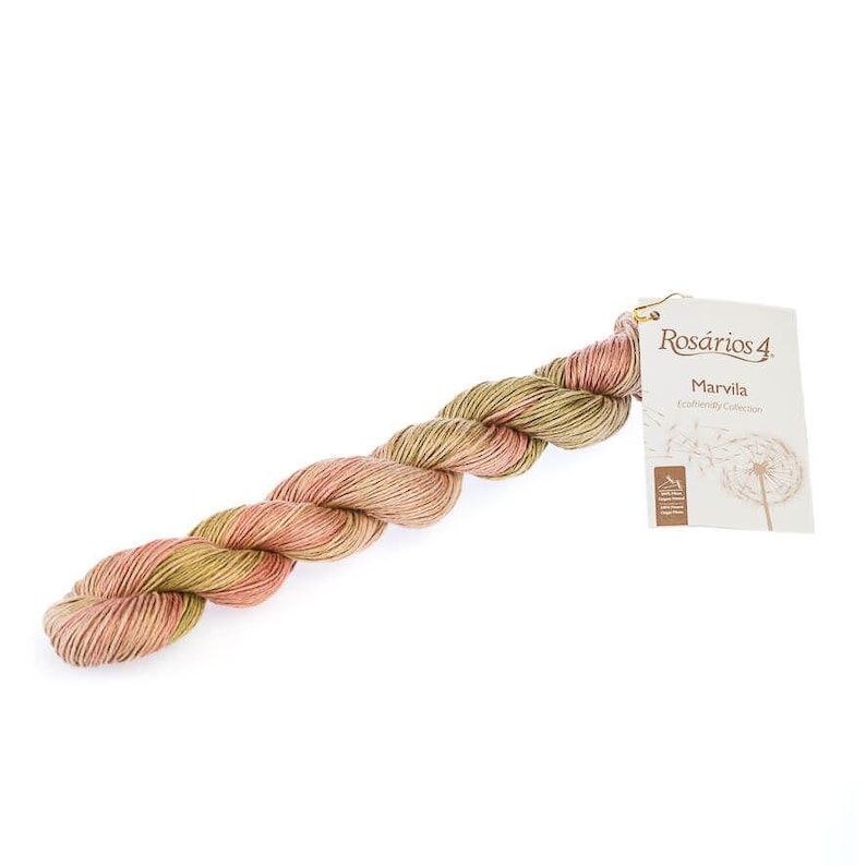 Puede incluir: Una madeja de hilo trenzada con una mezcla variada de fibras en rosa suave, verde oliva apagado y crema. Incluye una etiqueta de papel blanca con el texto Ros&aacute;rios 4, Marvila y Ecofriendly Collection, junto a un dibujo lineal de un diente de le&oacute;n.