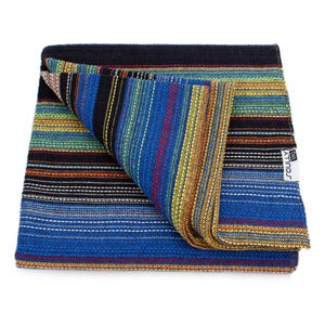 May include: A folded woven textile featuring a vibrant multi-colored striped pattern in shades of blue, black, yellow, green, and red. The fabric has a textured appearance and includes a white rectangular tag with the text SOULLY tag attached.