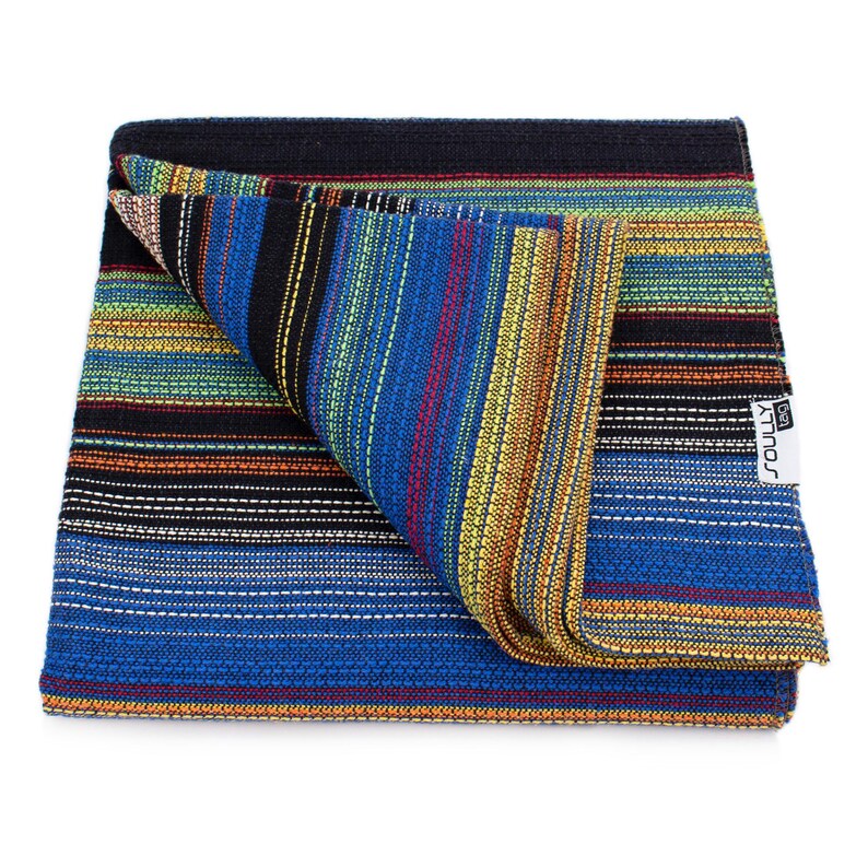May include: A folded woven textile featuring a vibrant multi-colored striped pattern in shades of blue, black, yellow, green, and red. The fabric has a textured appearance and includes a white rectangular tag with the text SOULLY tag attached.