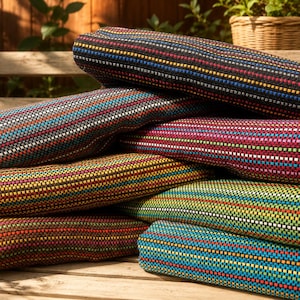 May include: A stack of folded woven blankets featuring a textured grid pattern. Each blanket displays a unique color palette, including combinations of black, blue, red, yellow, green, and pink threads, creating a vibrant, multi-colored striped effect.