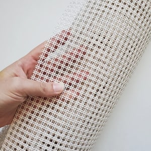 May include: White canvas mesh fabric with a grid pattern. The fabric is rolled up and held in a hand.