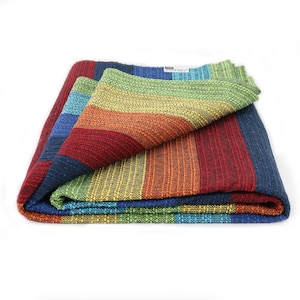 Pode incluir: Um sling de bebé tecido em riscas arco-íris, dobrado ao meio, com uma pequena etiqueta que diz "Didymos".