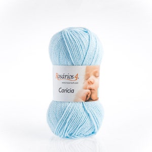 May include: A ball of light blue yarn with a label that reads "Rosários 4" and "Carícia". The label features an image of a baby's face. The yarn is a soft, pastel color.