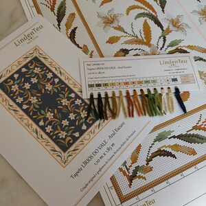May include: A close-up of a cross-stitch pattern kit for a tapestry called "LIRIOS DO VALE - Azul Escuro". The kit includes a colour chart with 15 different shades of yarn, a printed pattern, and a description of the design. The tapestry is 1.10 metres by 1.85 metres.