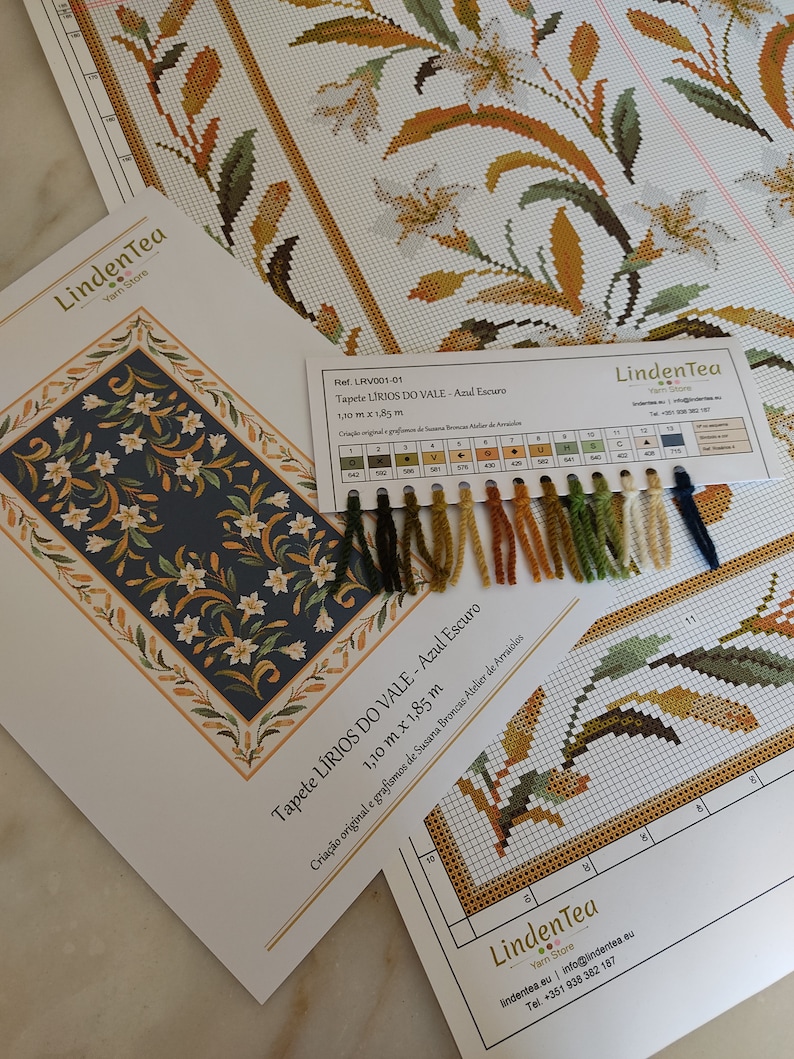 May include: A close-up of a cross-stitch pattern kit for a tapestry called "LIRIOS DO VALE - Azul Escuro". The kit includes a colour chart with 15 different shades of yarn, a printed pattern, and a description of the design. The tapestry is 1.10 metres by 1.85 metres.