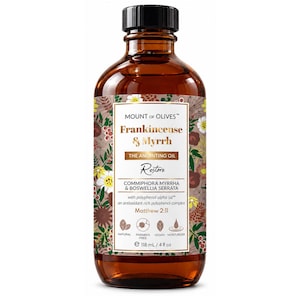 May include: An amber glass bottle of Mount of Olives Frankincense & Myrrh anointing oil. The label features floral illustrations, the text Restore, Matthew 2:11, and icons for natural, paraben free, vegan, and moisturizer. Volume is 4 fl oz.