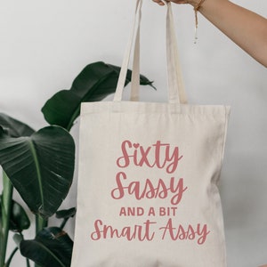 May include: A white canvas tote bag with the text "Sixty Sassy and a bit Smart Assy" in pink lettering.