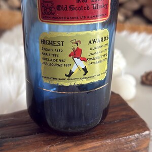 May include: A blue glass with Johnnie Walker Red Label Old Scotch Whisky labels. The labels list awards from various cities and the text "Guaranteed Same Quality Throughout The World."