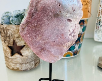 May include: A pink and white agate slice on a black metal stand. The agate has a natural, rough edge and is translucent.