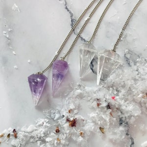 May include: Three crystal pendulums on silver chains. Two are clear quartz and one is amethyst.