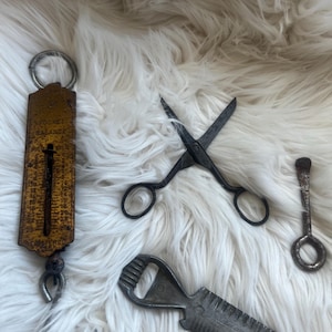 May include: A collection of vintage metal tools including a yellow rectangular pocket balance scale with a hook, a pair of dark iron scissors, a small metal key-like tool with a ring handle, and a multi-functional bottle opener tool with a serrated edge.
