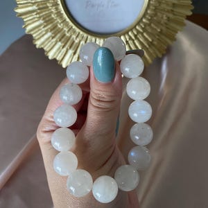 Könnte beinhalten: Weißes Mondstein-Armband mit runden Perlen. Das Armband befindet sich am Handgelenk einer Person.