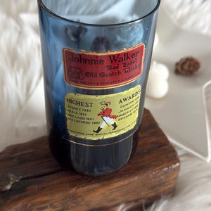 May include: A blue glass with "Johnnie Walker Red Label Old Scotch Whisky" labels. The labels include text about awards and locations. The glass is on a wooden base.