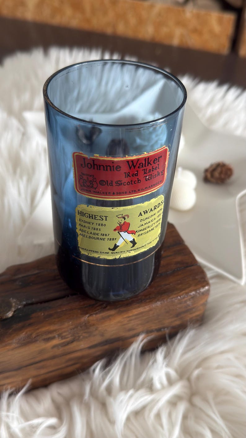 May include: A blue glass with "Johnnie Walker Red Label Old Scotch Whisky" labels. The labels include text about awards and locations. The glass is on a wooden base.