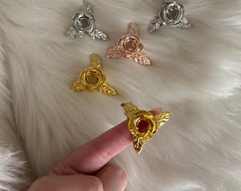 May include: Four decorative rose-shaped candle holders in gold, silver, and rose gold. Each holder has three leaves and a circular centre.