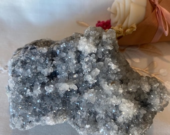 May include: A cluster of gray and white crystals with a rough, natural texture. The crystals are arranged in a random pattern, creating a unique and interesting display.