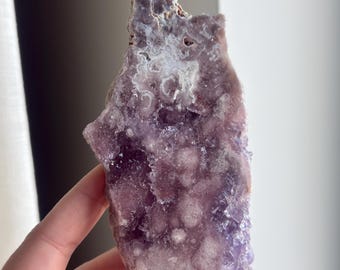 May include: A purple amethyst crystal with a unique, bubbly texture, displayed on a black metal stand.