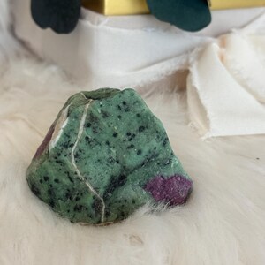 Puede incluir: Una piedra preciosa verde y rosa en bruto con una forma irregular y rugosa. La piedra tiene una base verde con inclusiones rosas y blancas.