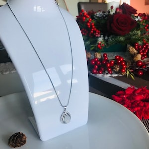 Könnte beinhalten: Eine silberne Kettenkette mit einem tropfenförmigen Anhänger, der einen weißen Stein enthält, der von kleineren klaren Steinen umgeben ist.