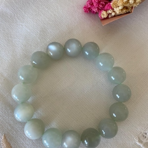 Könnte beinhalten: Ein hellgrünes Jadearmband mit runden Perlen. Die Perlen haben einen dezenten Schimmer.