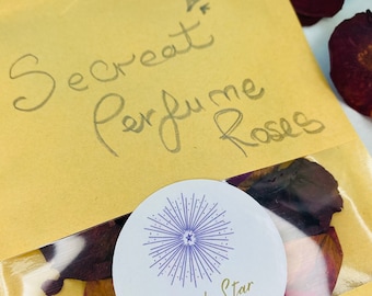 May include: A yellow paper bag with the words "Secret Perfume Roses" written on it. The bag contains dried rose petals and a white circle sticker with the words "Purple Star" and "Believe in your inner strength".