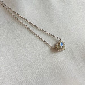 Könnte beinhalten: Eine silberne Kettenkette mit einem herzförmigen Anhänger, der einen blauen Edelstein enthält, der von kleineren klaren Edelsteinen umgeben ist.