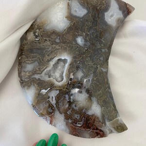 May include: A crescent moon shaped agate slice with brown, white, and gray swirling patterns. The agate has a natural, rough texture and a smooth, polished surface.