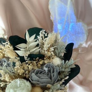 Könnte beinhalten: Ein Strauß getrockneter Blumen in einer Schachtel, mit einer Auswahl an getrockneten Blumen und Grün, darunter weiße, beige und grüne Blumen sowie eine hellgrüne und eine hellgraue Kerze in Rosenform.