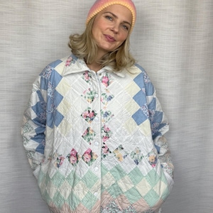 May include: A quilted jacket featuring a patchwork design of white, light blue, and pastel green diamond-shaped fabric panels with floral patterns, a pointed collar, and a front snap-button closure, paired with a gradient pink and yellow beanie.