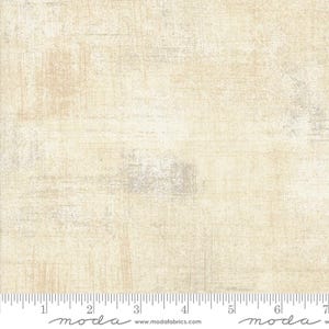 Peut inclure: Un gros plan sur un tissu beige avec un motif texturé subtil. Le tissu a un aspect légèrement vieilli, avec des nuances de gris et de blanc. Le tissu est mesuré en pouces avec le texte "moda" imprimé sur la règle.