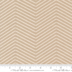 May include: Beige fabric with a white chevron pattern. The fabric is textured and has a subtle sheen. The fabric is shown with a ruler for scale.