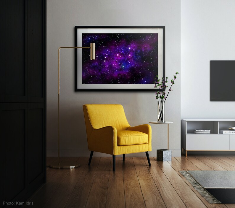 May include: A yellow armchair with a black metal frame sits in a living room with a black and white floor. A gold floor lamp stands next to the chair. A framed print of a galaxy with purple and blue hues hangs on the wall above a small side table.