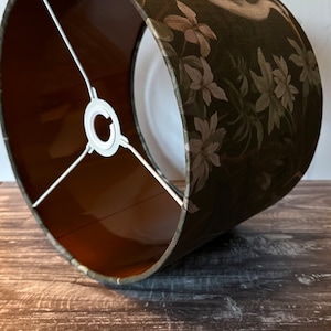 May include: A green lampshade with a floral pattern and a white bird design. The lampshade has a brown lining and a white metal frame.
