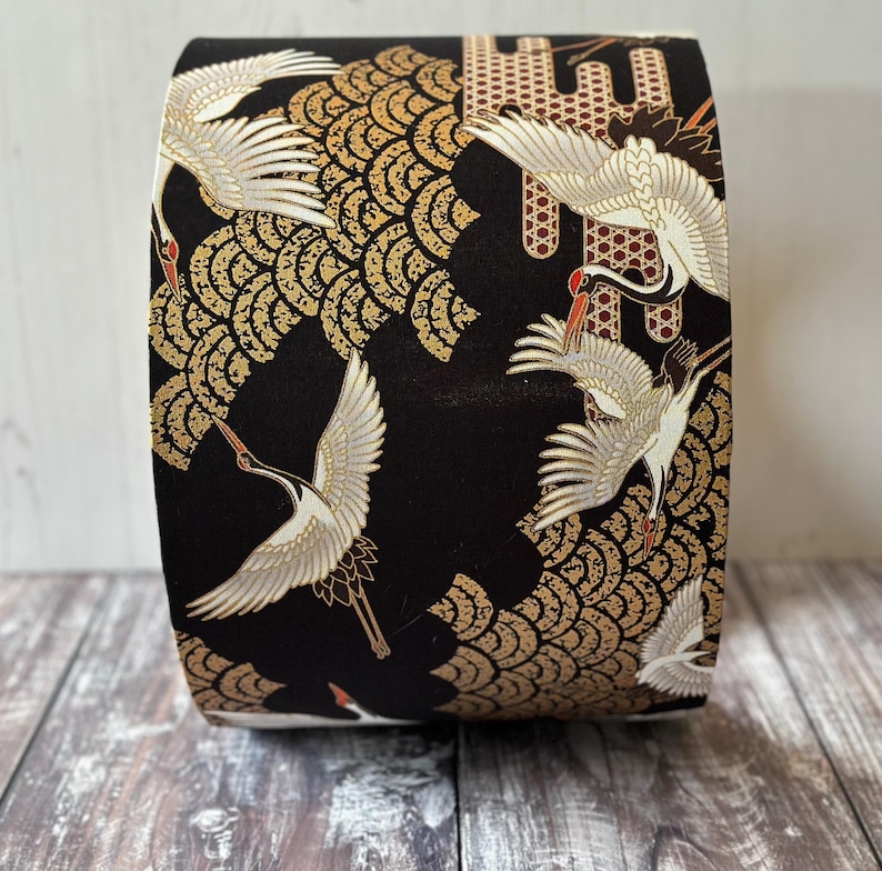 May include: Drum lampshade with a repeating pattern of white cranes, gold and red accents. The cranes are in flight against a backdrop of gold fan-shaped designs.