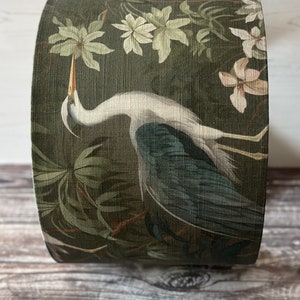 May include: A green lampshade with a white heron and floral pattern. The heron is standing in a swamp with green foliage and white flowers.