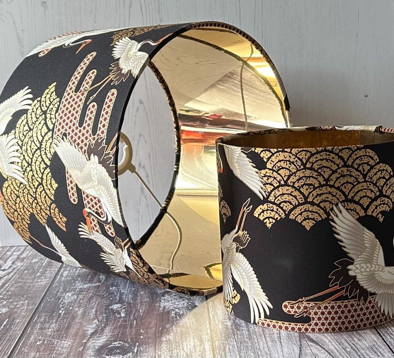 May include: Two black lampshades with a gold interior and a Japanese crane design. The exterior features white cranes, gold fan-shaped patterns.