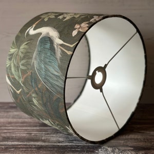 May include: A green and blue lampshade with a white interior. The lampshade features a large bird with a long neck and a floral pattern.