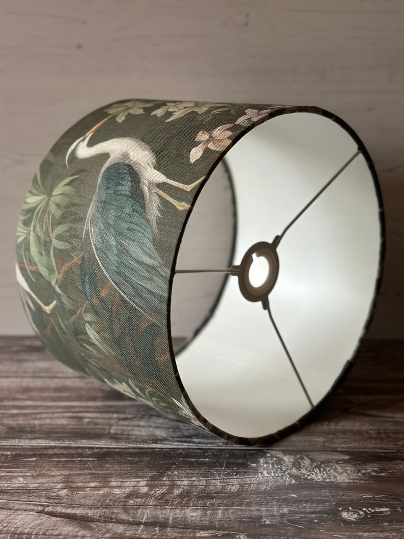 May include: A green and blue lampshade with a white interior. The lampshade features a large bird with a long neck and a floral pattern.