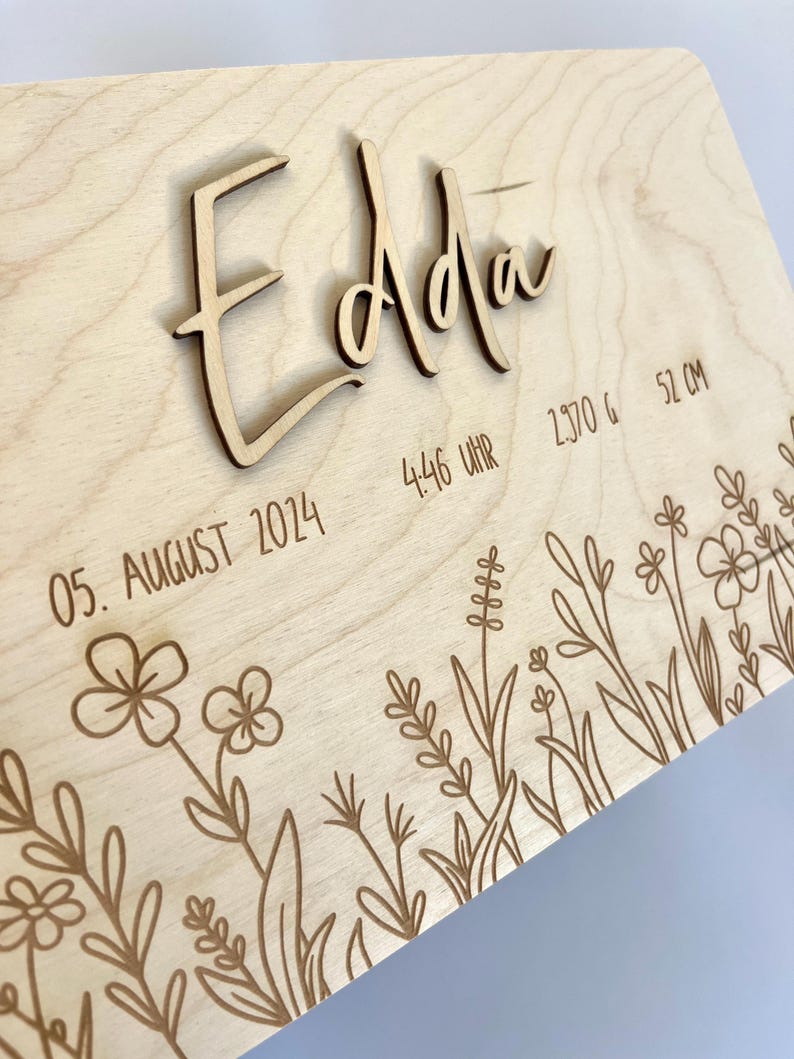 May include: A wooden plaque with the name "Edda" engraved in cursive script. The plaque also includes the date "05. August 2014", the time "4:46 Uhr", the weight "2370 g", and the length "51 cm". The plaque is decorated with a floral design.